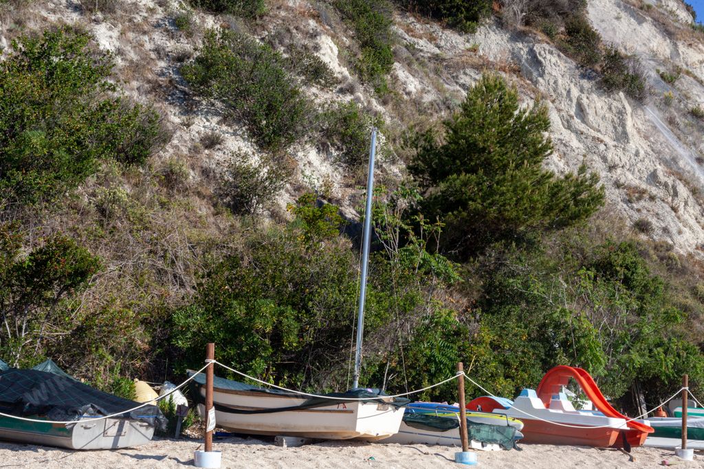A bright summer morning in Numana, Italy with small boats docked on the sand in front of a big hill