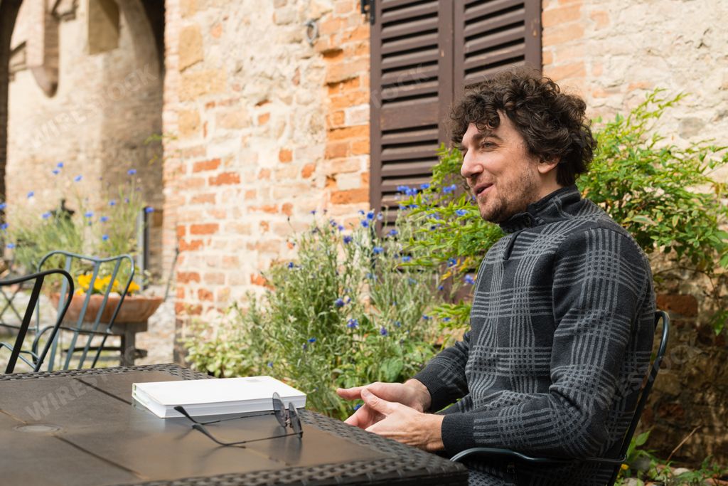 A young Italian man with curly hair sitting in the quiet open-air restaurant