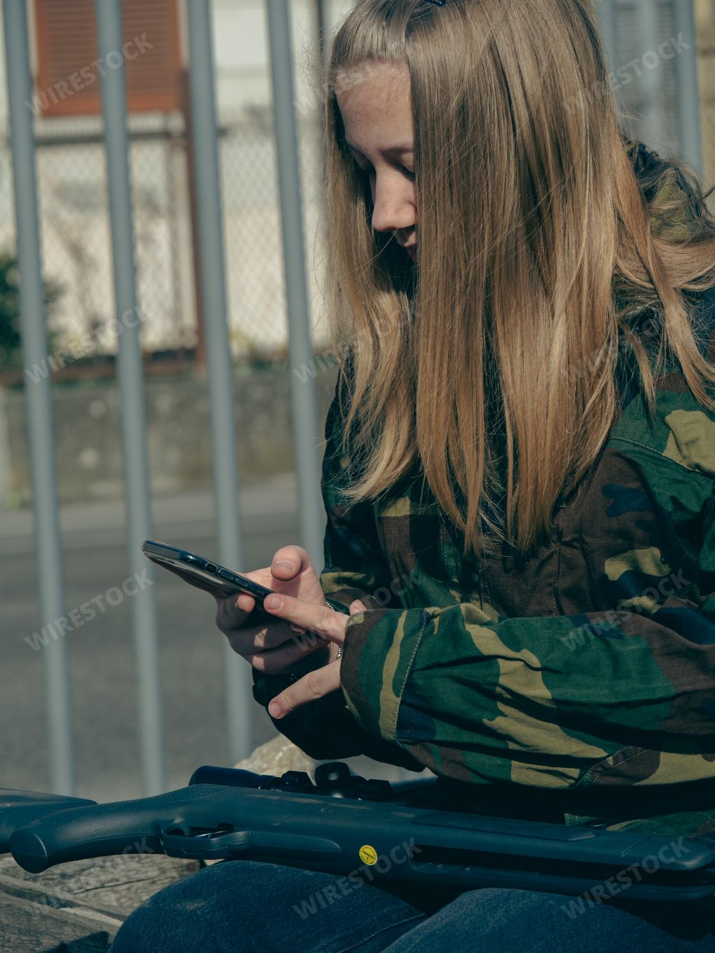 A female soldier in camouflage holding rifle and smartphone during Russia and Ukraine collision outdoors