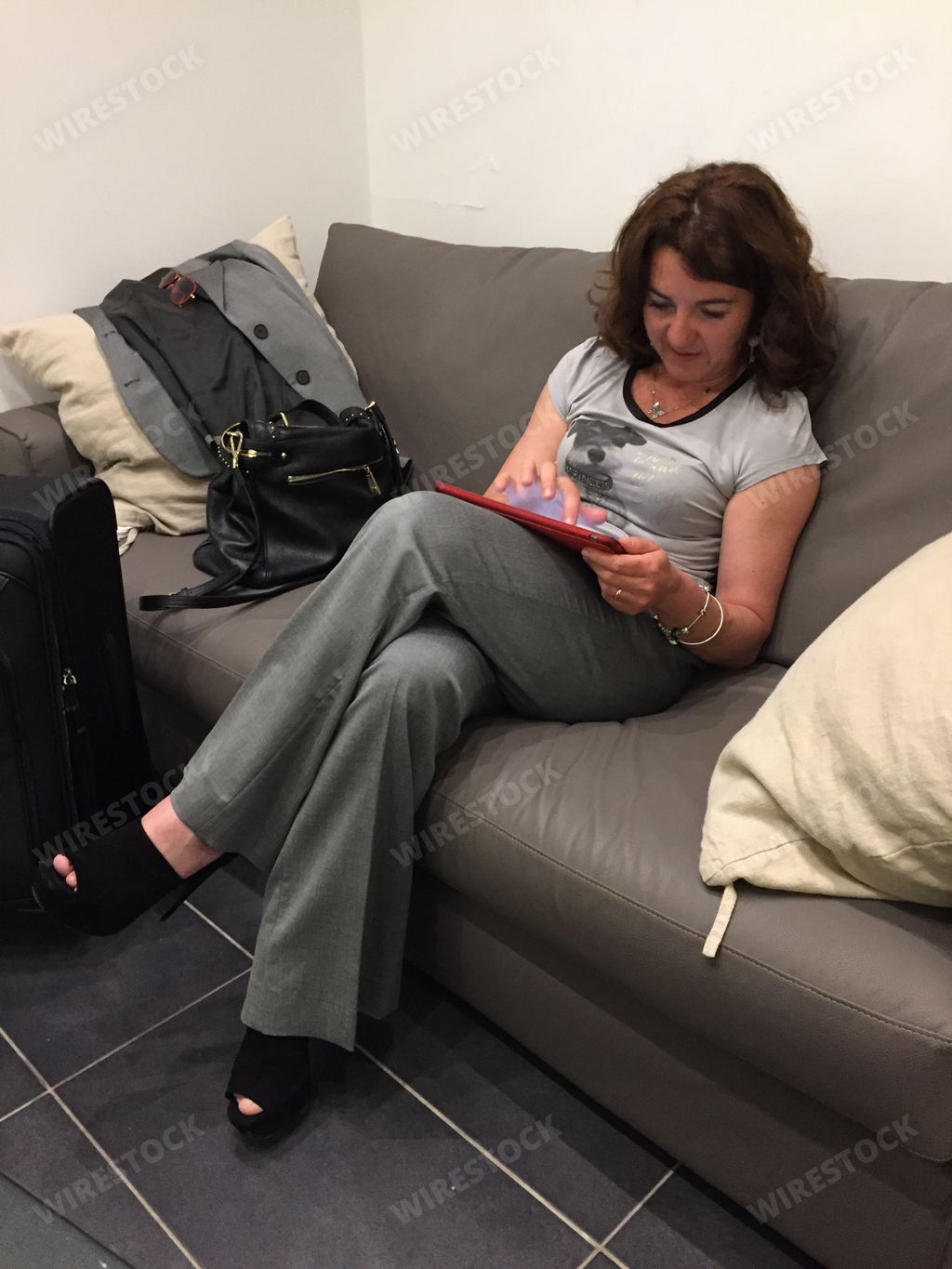 a vertical shot of a middle-age female sitting cross-legged on a sofa and using her tablet