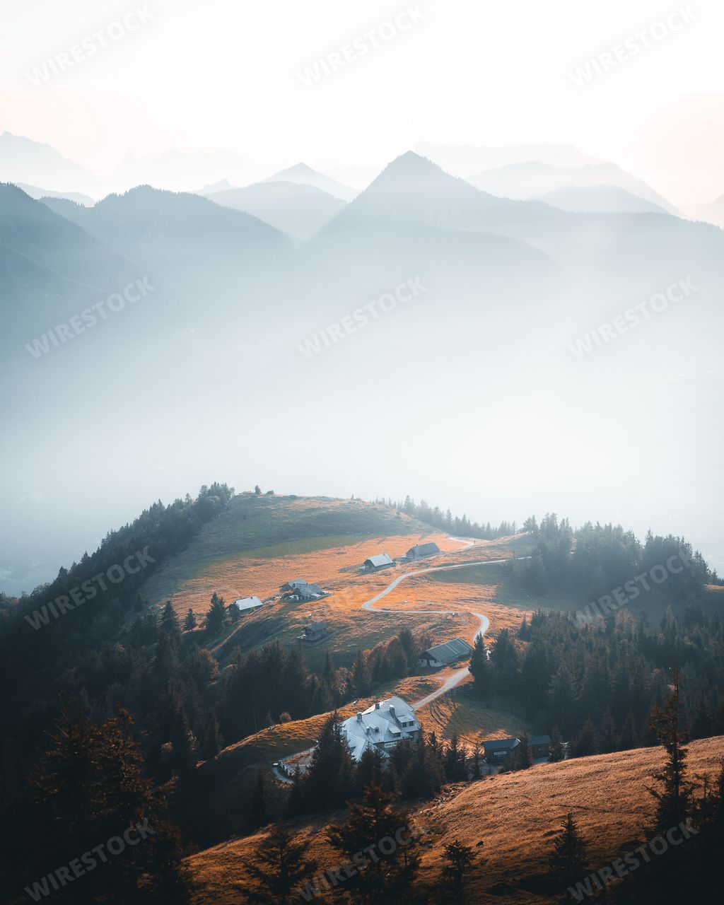 A vertical shot of a green hill with roads, homes, and trees in the background of mountains