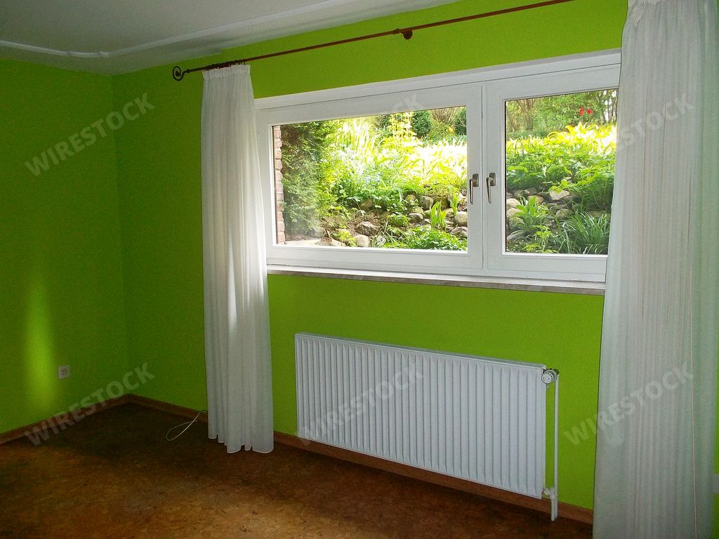 A window with open white curtains in a room with green walls with a view to the garden