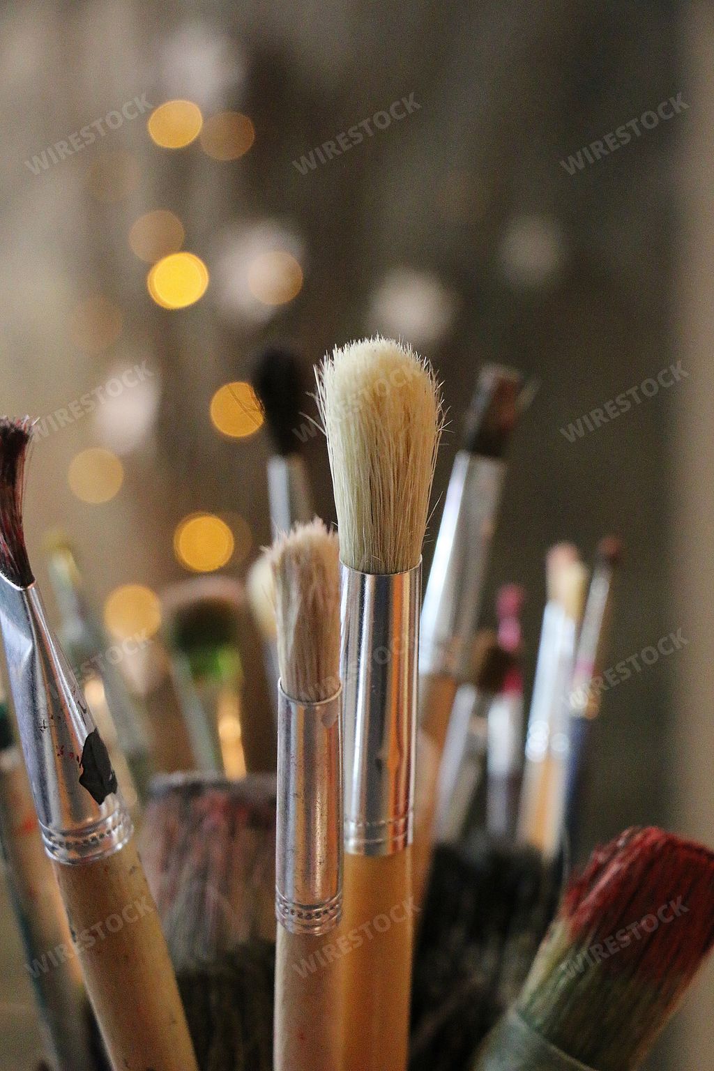 A vertical selective focus closeup shot of different types of paint brushes with bokeh lights on the background