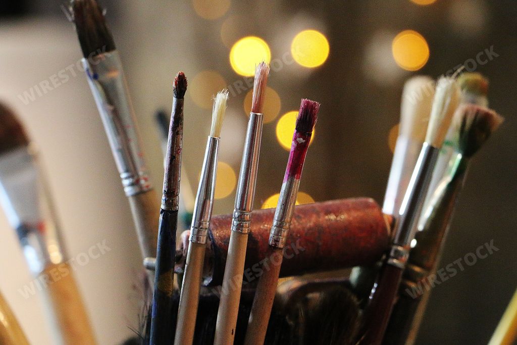 A selective focus closeup shot of different types of paint brushes with bokeh lights on the background