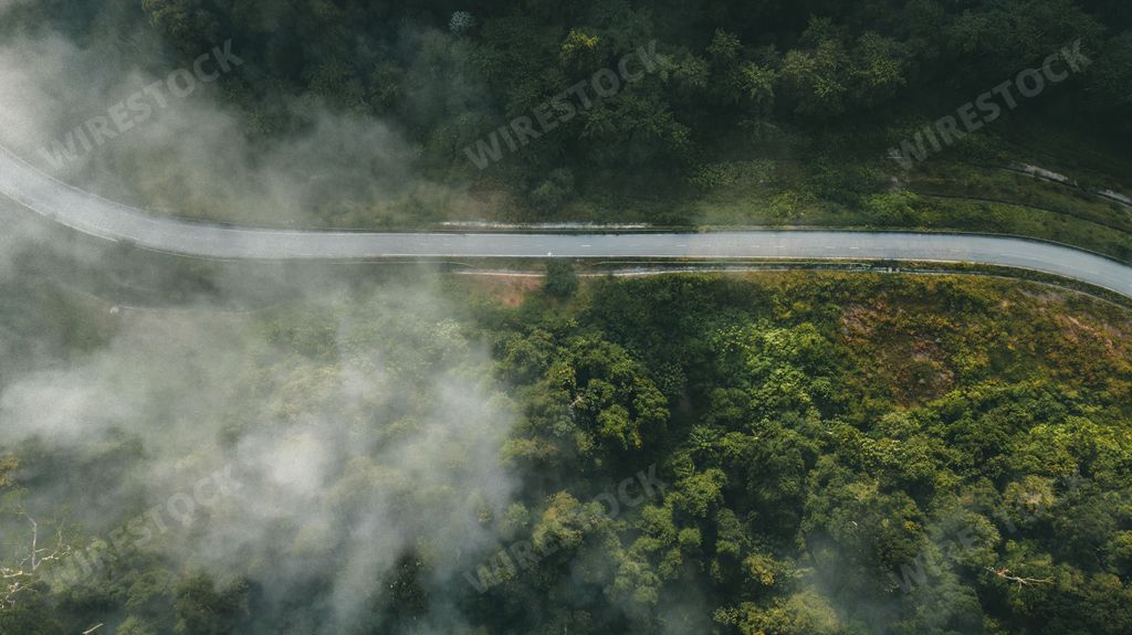 An aerial view of a winding road surrounded by a lush green landscape with trees in the distance.
