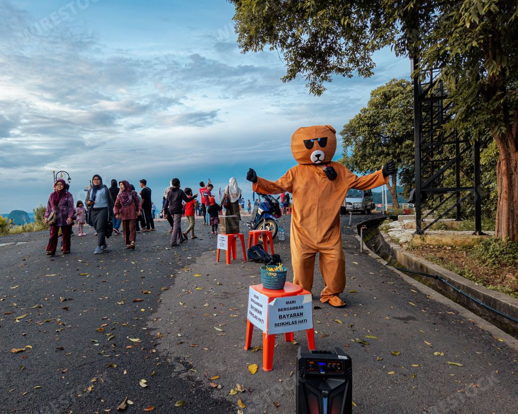 A male performing a joyful dance wearing a bear-themed costume at the scenic Wang Kelian lookout point
