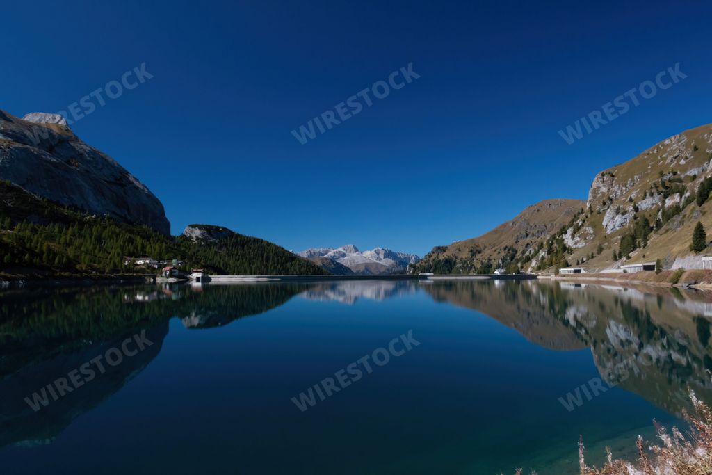 A scenic view of houses and green mountains reflecting in Fedaia Lake, Canazei, Italy