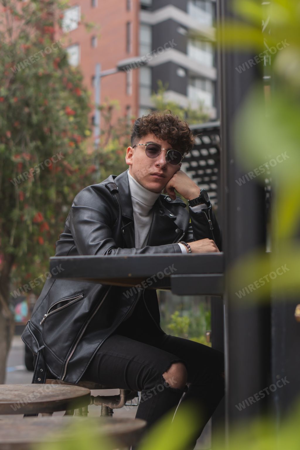 An attractive Latino man with curly hair and sunglasses sitting outdoors