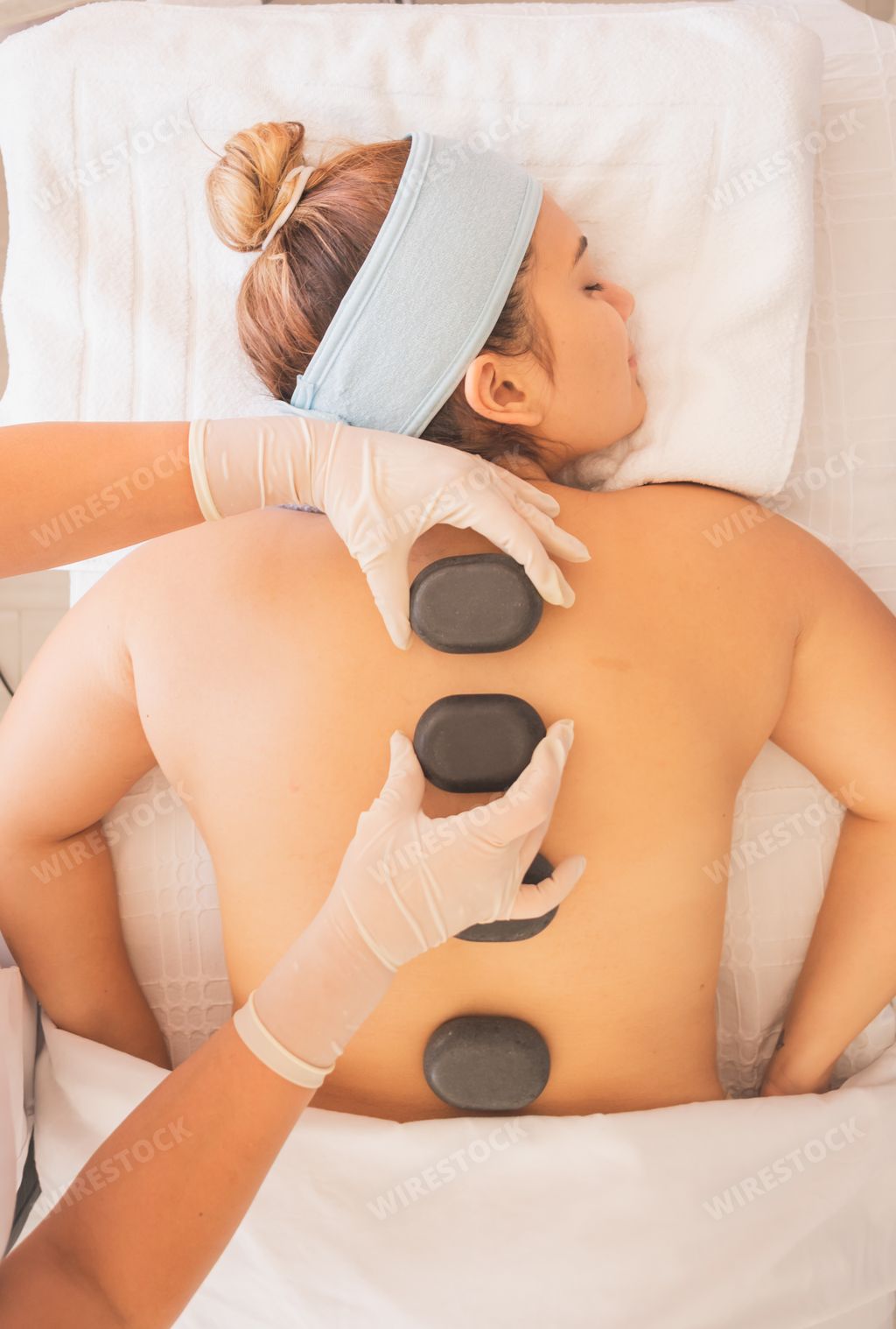 A vertical shot of a Hispanic female getting a hot stone massage at a spa