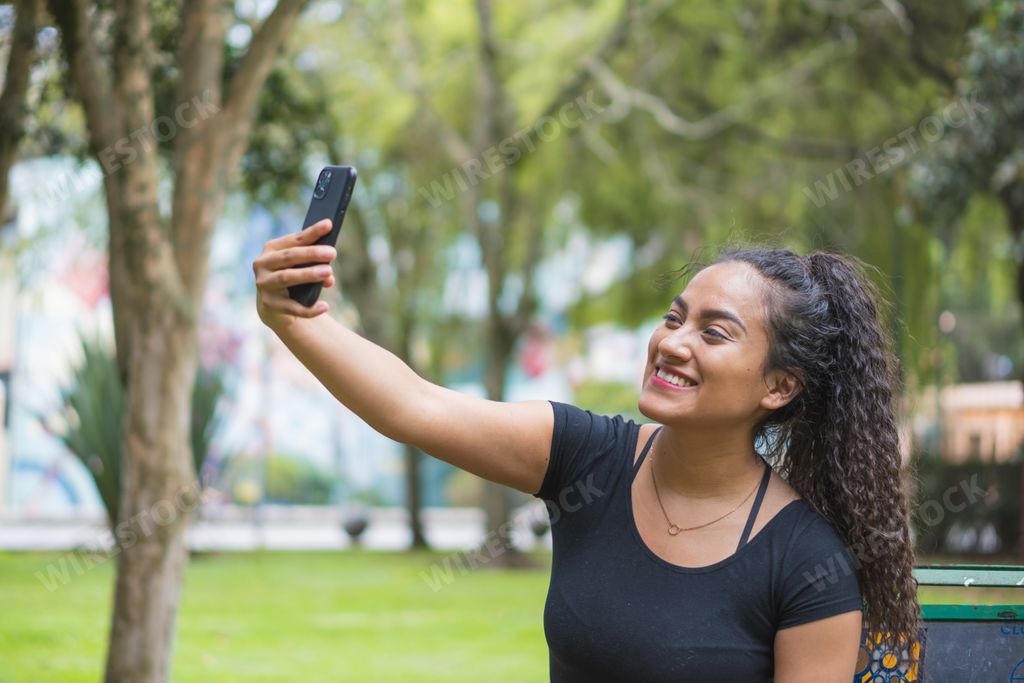 A Hispanic young female taking a selfie in a park