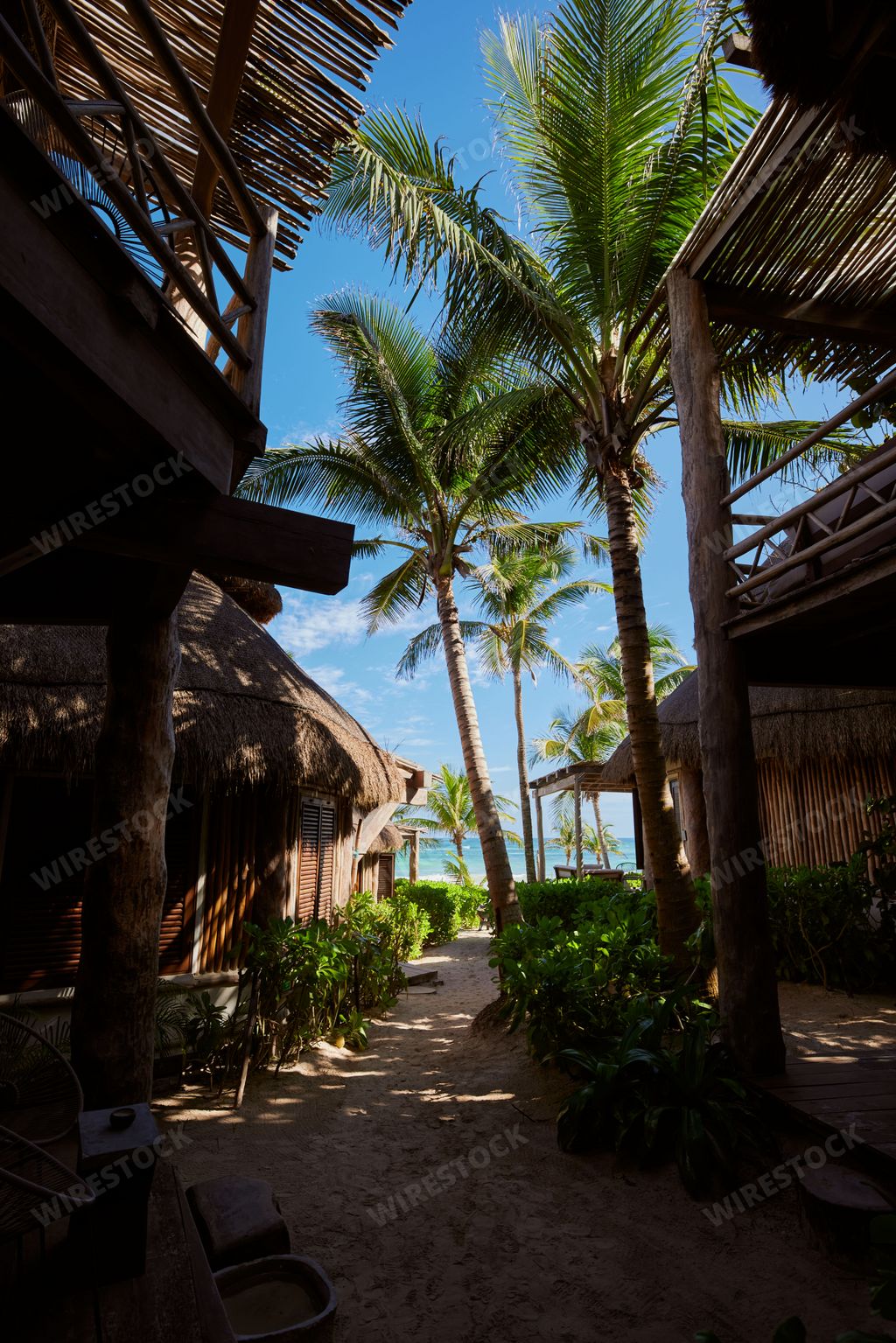 A vertical shot of tall palm trees and summer huts in Tulum, Mexico under a bright blue sky