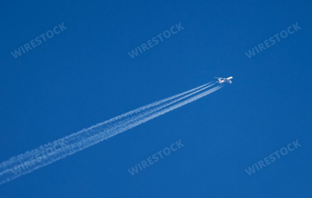 The low-angle view of an aircraft flying away with contrails in the blue sky