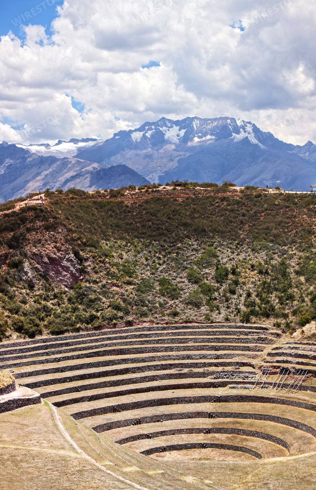 A vertical shot of circular terraces at Moray Inca Ruins near Cusco, Peru with mountains and clouds in the background