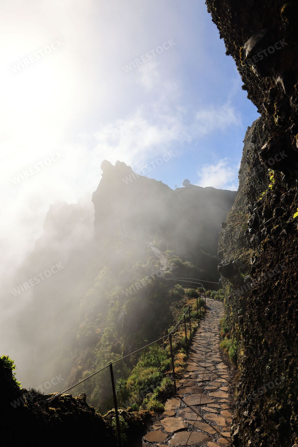 Scenic mountain path with stone steps leading through misty cliffs under a clear blue sky