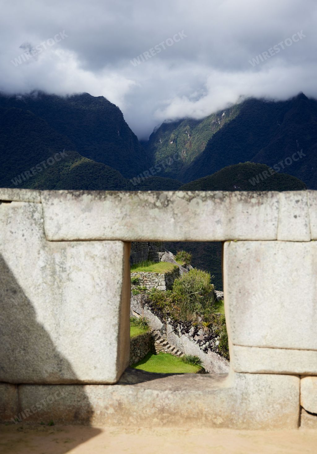A vertical shot of the Temple of the Three Windows ruins of Machu Picchu with clouds covering the hills in background