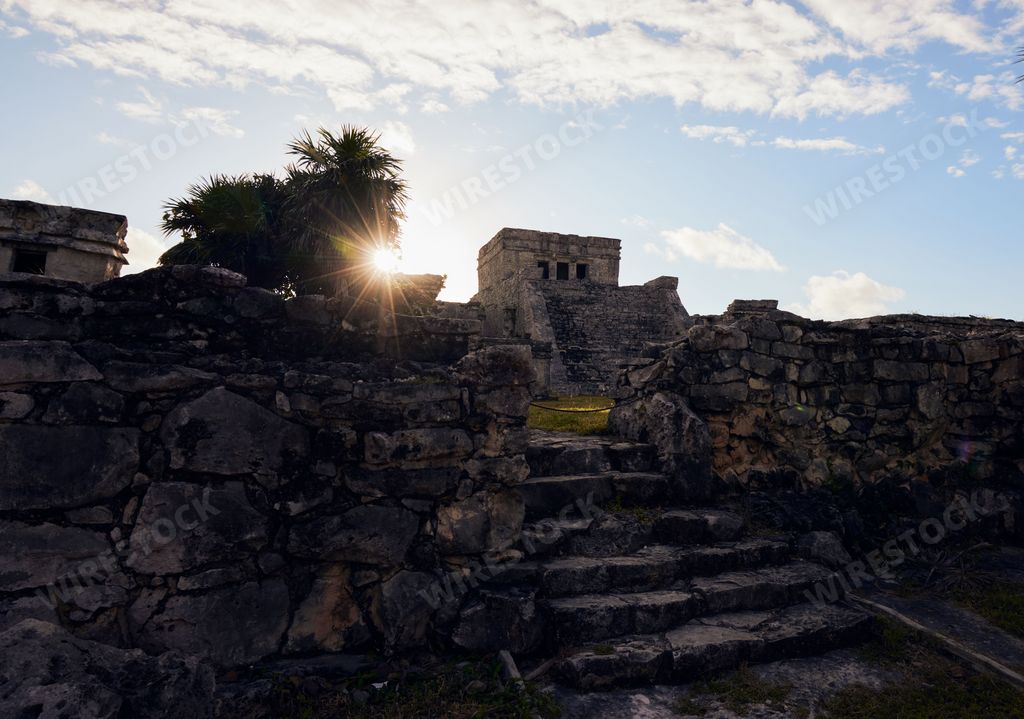 A scenic shot of the Tulum ruins with the bright sun shining in the background in Mexico