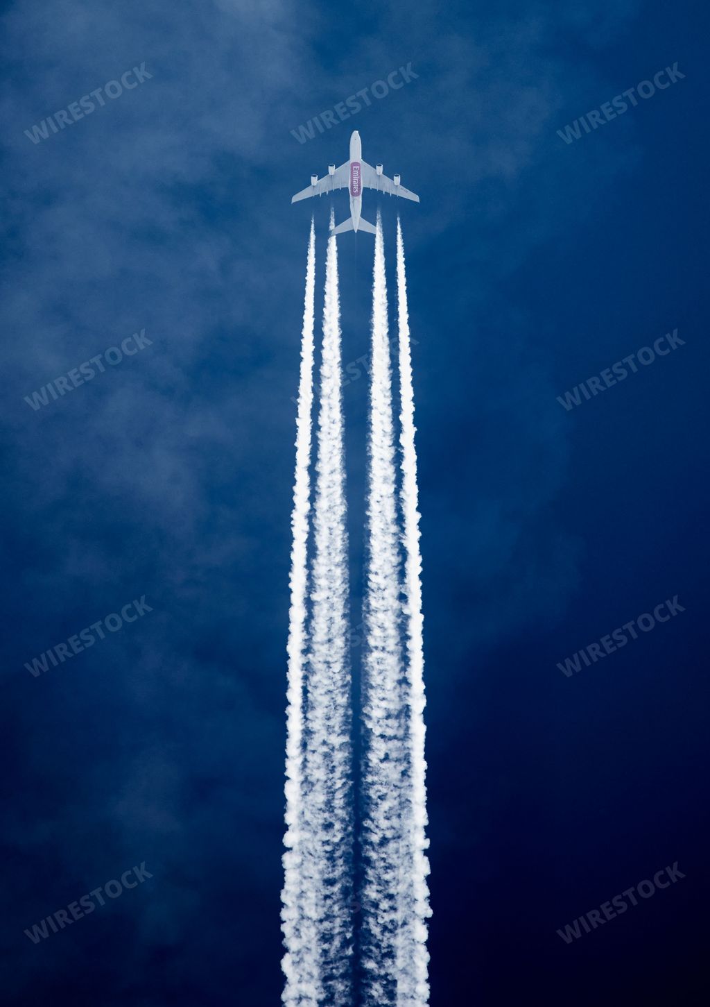 The vertical low-angle view of an aircraft with contrails in the blue sky