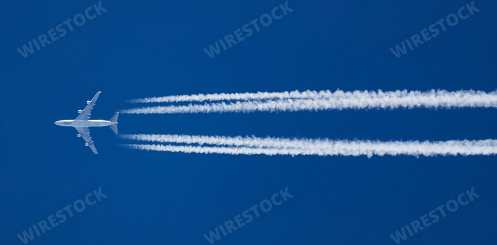 A white aircraft at a distance and contrails in clear blue sky