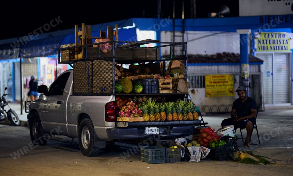 A fruit vendor selling fruits from the back of his pickup truck parked on the side of the street