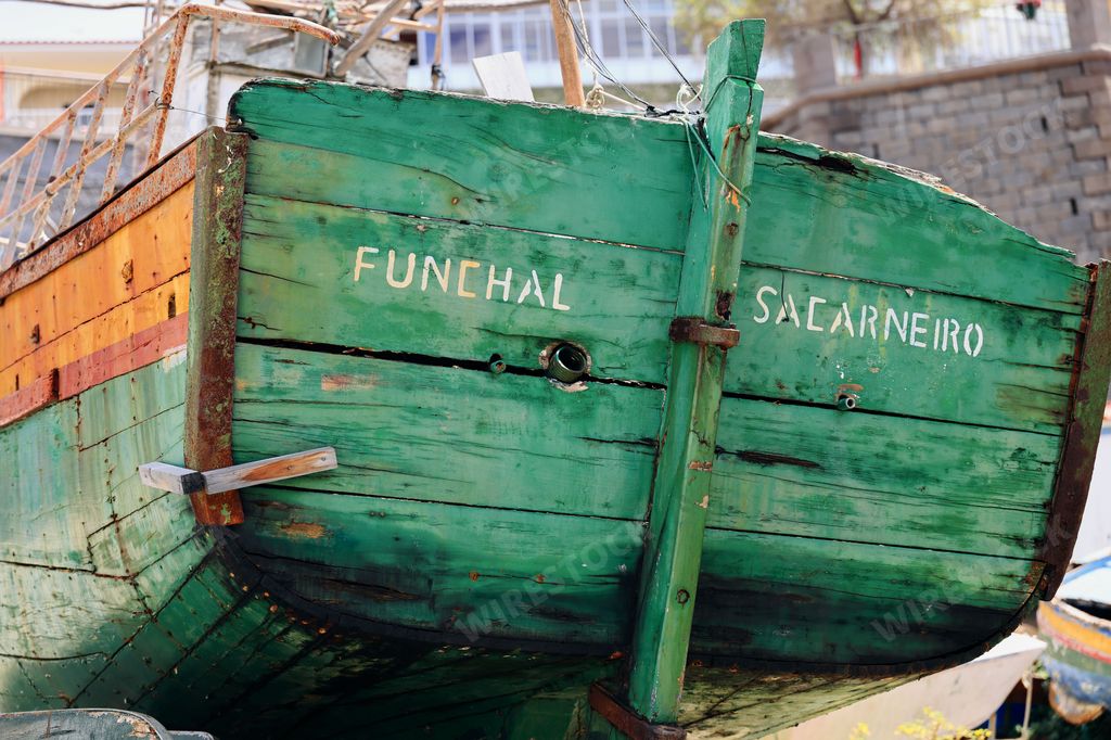 Close-up of an old green wooden boat with the names Funchal and Sacarneiro painted on it, docked at a harbor.