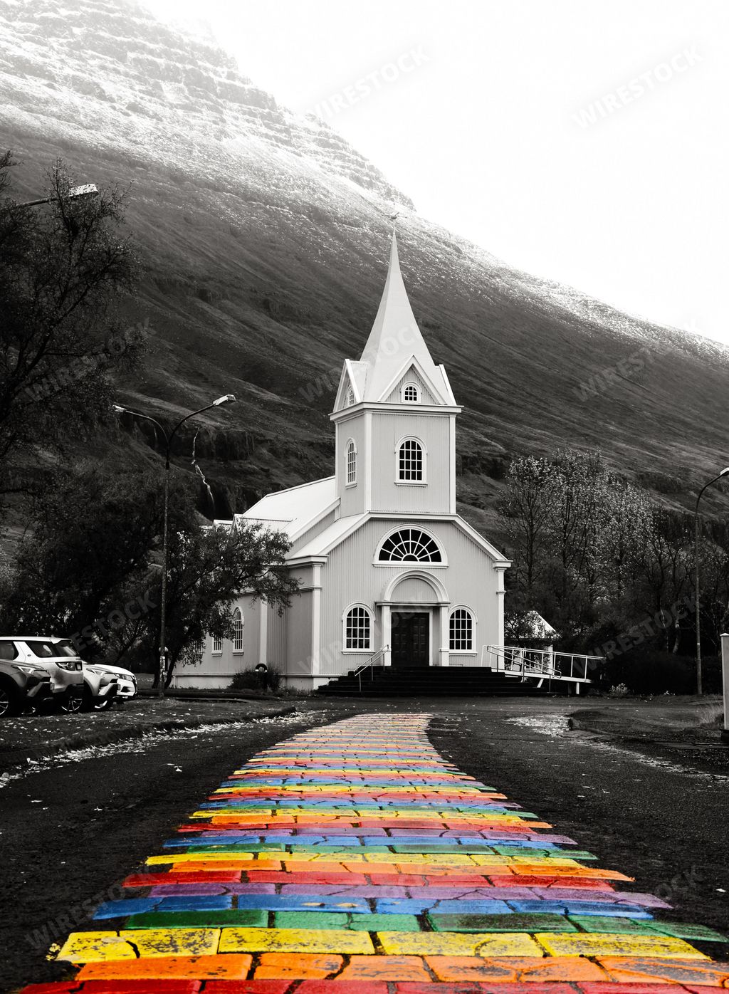 A grayscale vertical shot of rainbow walkway street with white church in Seyoisfjorour, Iceland