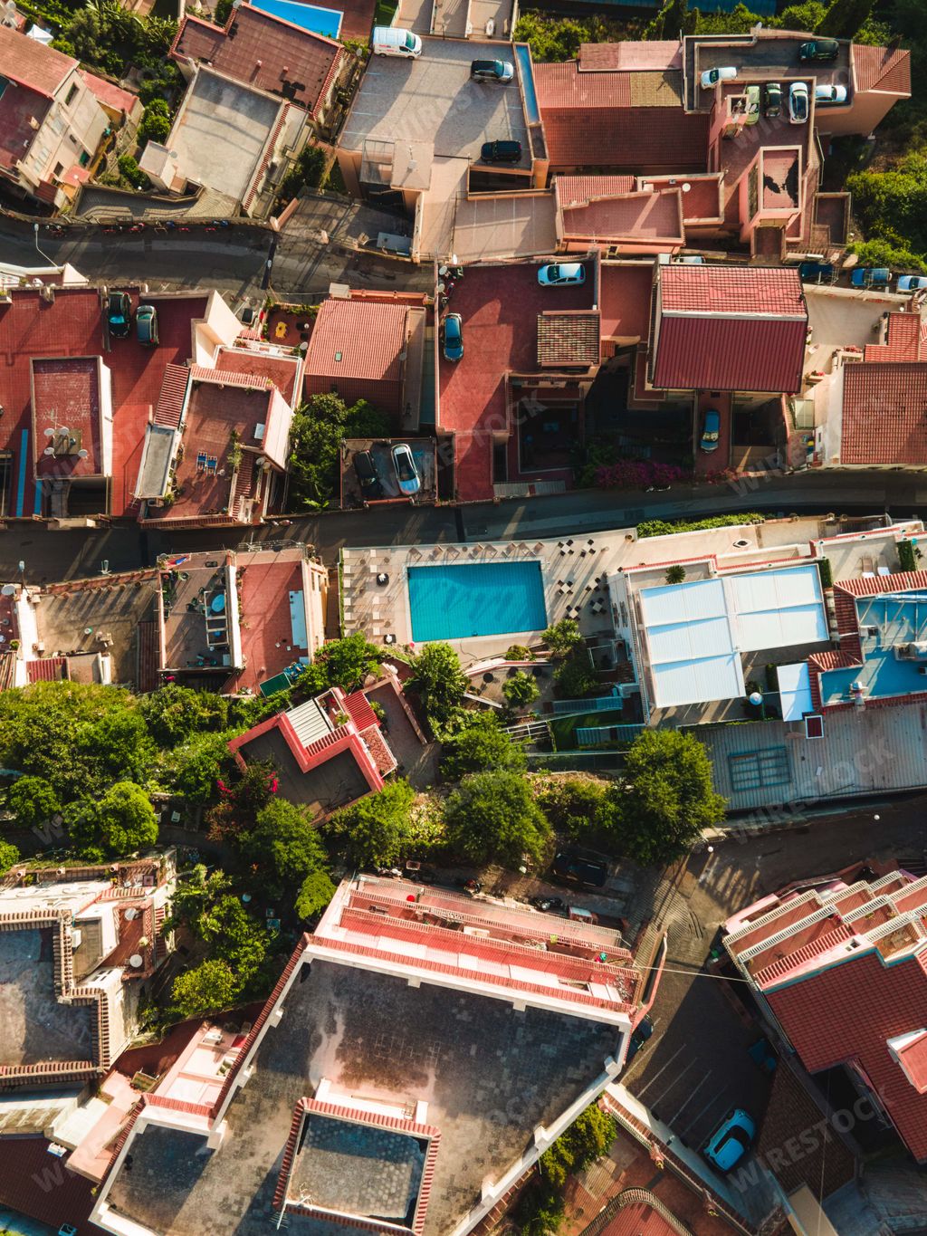 A vertical aerial shot of buildings with a pool and green trees in Taormina, Sicily