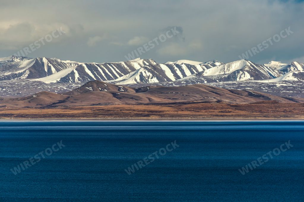 A gorgeous view of Lake Rakshastal in tibet, China with snowy peaks in the distance under a cloudy sky