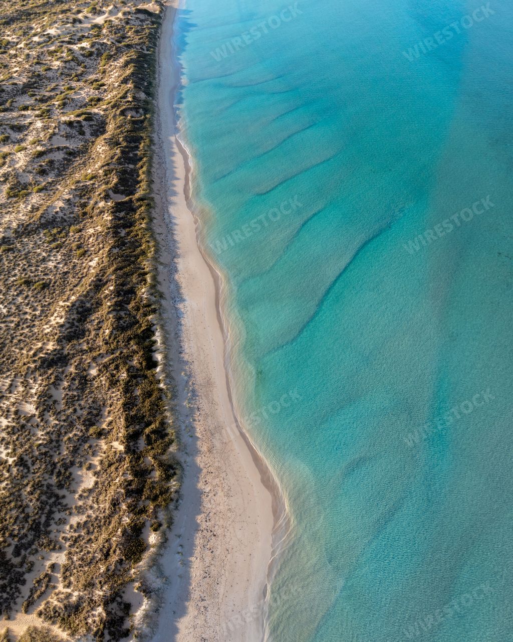 Aerial view of a pristine beach with clear turquoise water and sandy shoreline.
