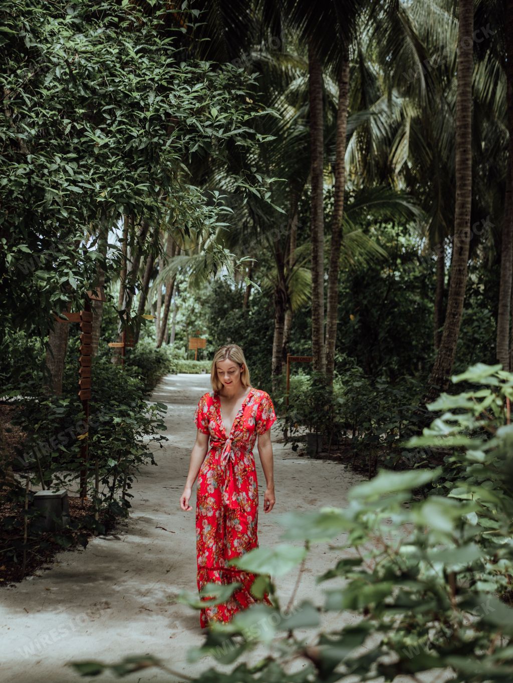A young woman in a red floral dress walking through a lush tropical garden