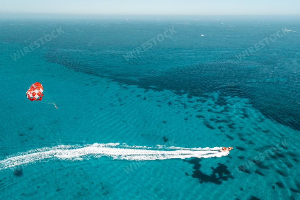 Aerial view of parasailing over clear turquoise waters with a speedboat pulling the parachute.