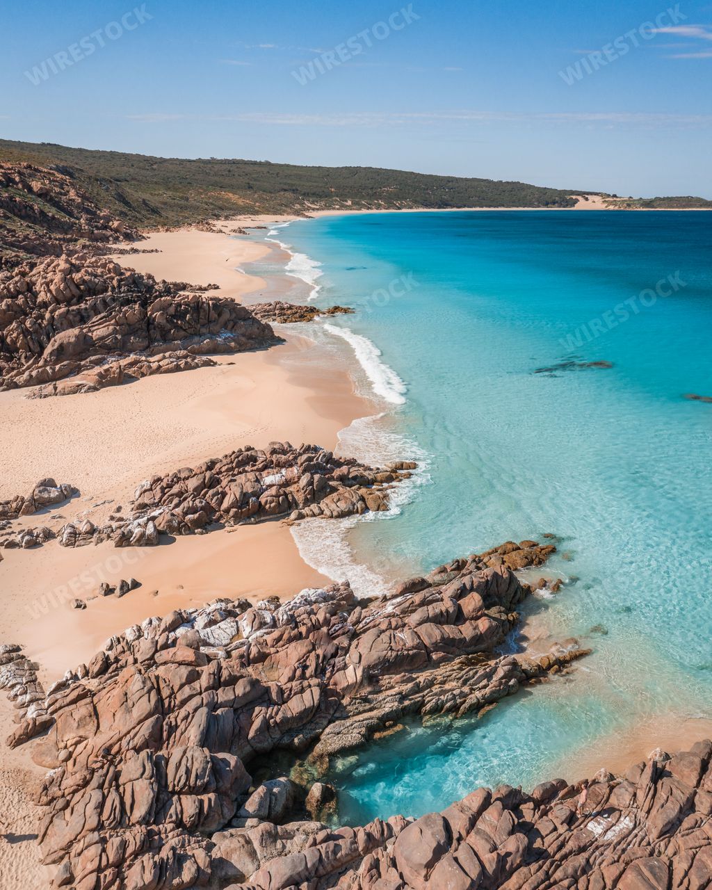 A vertical aerial drone shot of a heavenly sandy beach with cliffs and the crystal clear ocean water