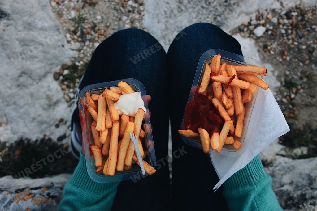 A high angle shot of a person holding two boxes of french fries with ketchup and mayo
