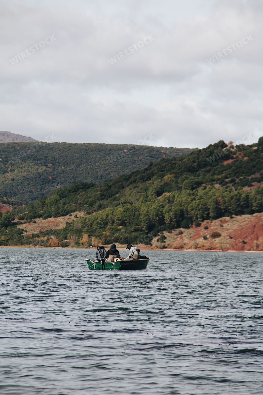 A vertical shot of people on a boat sailing in the sea with mountains in the background