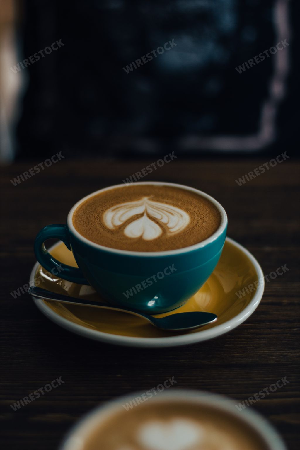 A vertical selective closeup shot of coffee with latte art in a blue ceramic cup on a wooden table