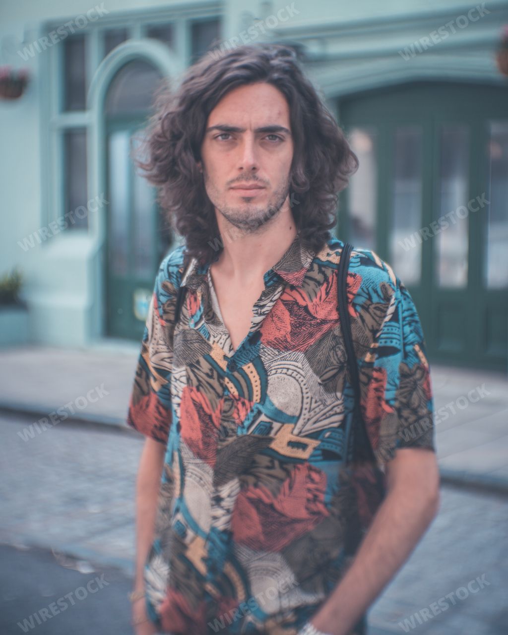 A young Spanish man with long hair and a colorful shirt in the street on a sunny day