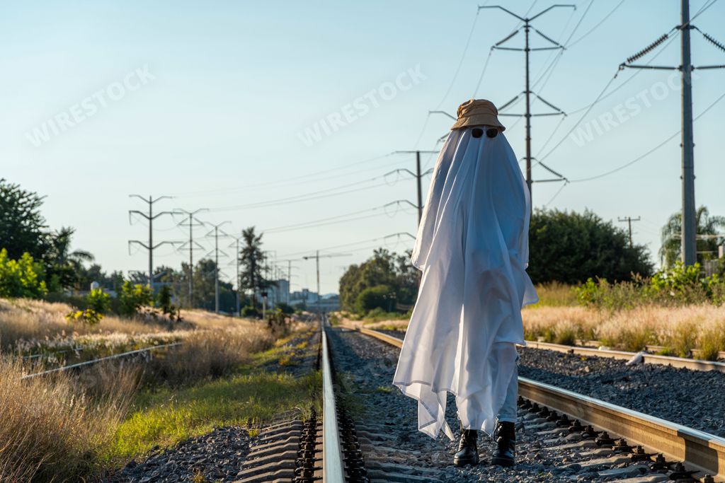 A person in a funny ghost costume with a white sheet, sunglasses, and a yellow hat walking around