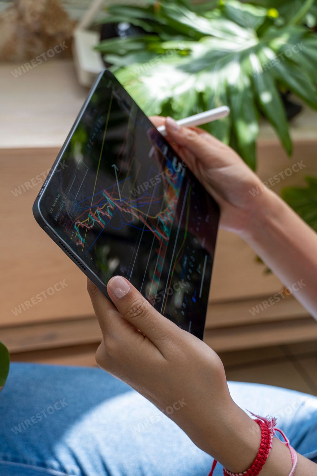 A vertical shot of a young lady trading crypto currencies online and stocks with her tablet