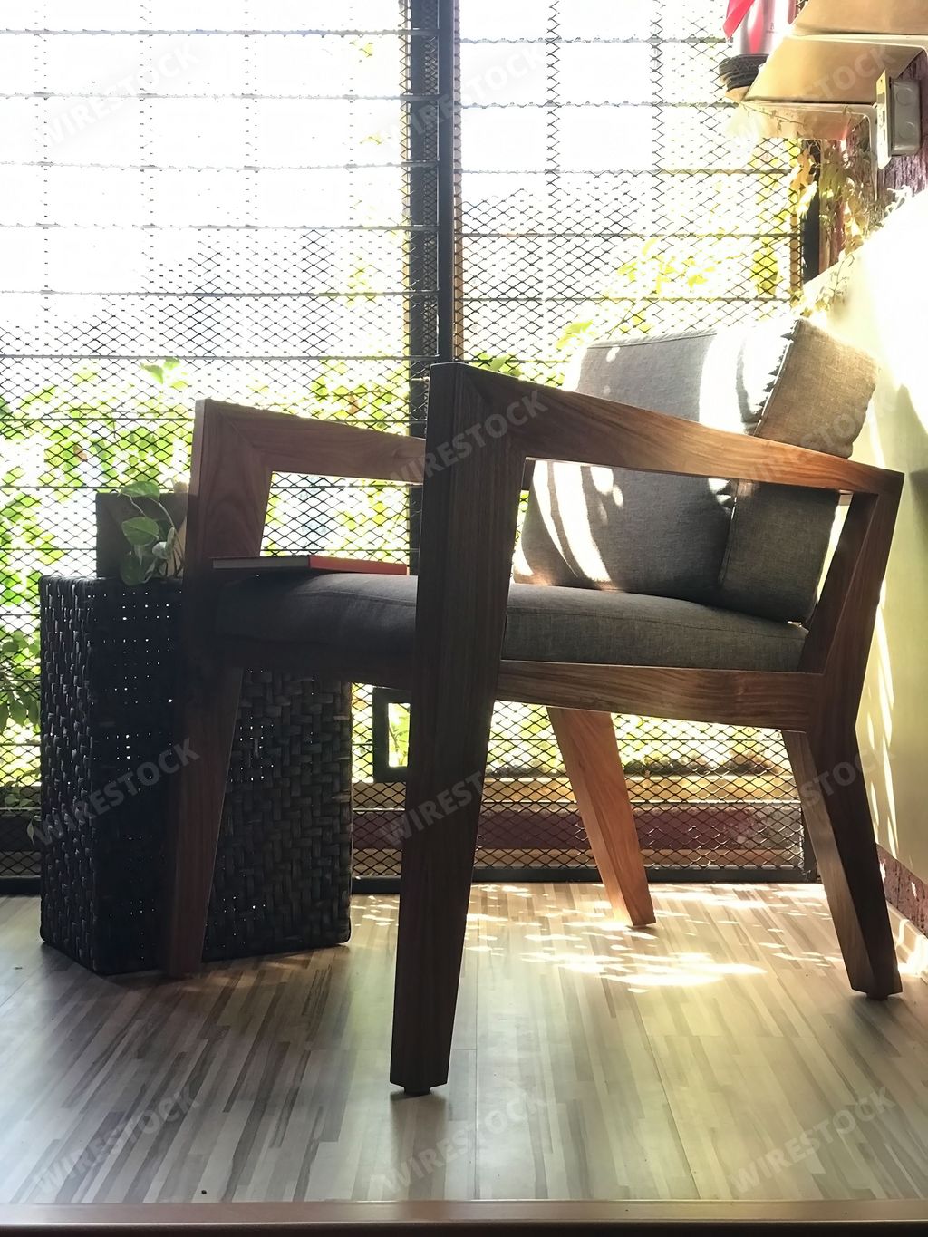 A comfortable wooden black armchair in the room next to a table, window and plants with sun rays and shadow on it