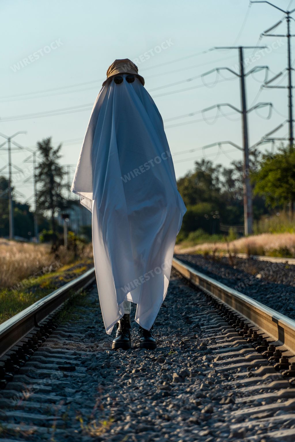 A vertical shot of a person in a funny cute ghost costume with a sheet, a hat, and sunglasses