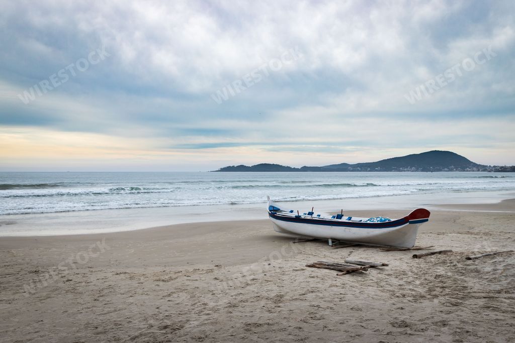 A scenic view of the sea with a boat isolated on the sandy beach under the cloudy sky