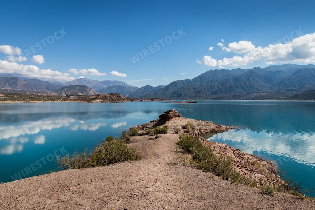 The cloudy sky reflected in a lake surrounded by mountains in a rural area