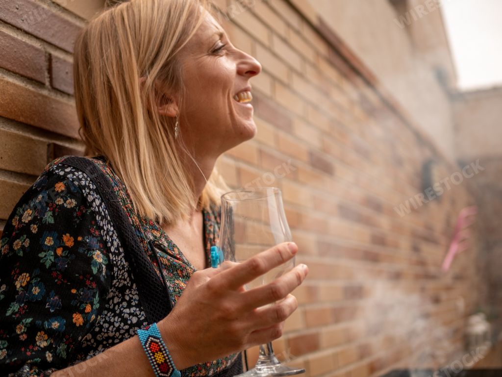 A happy Spanish blonde woman with a glass of white wine leaning against a wall in the backyard of her house