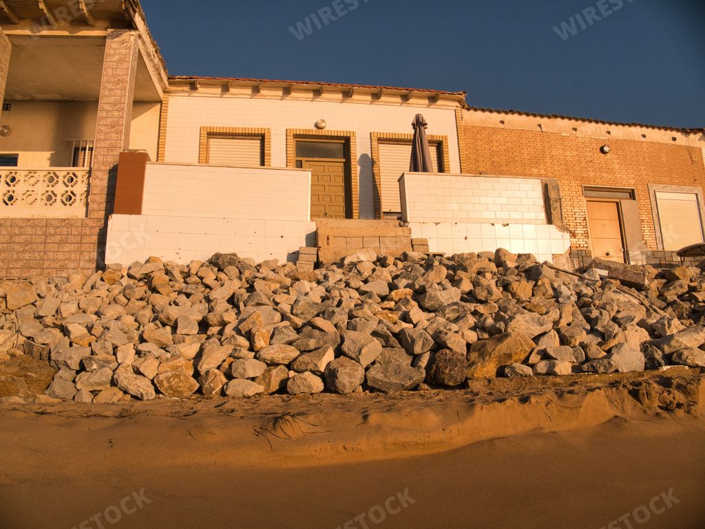 An old stone house with rocks on a sandy beach at sunset