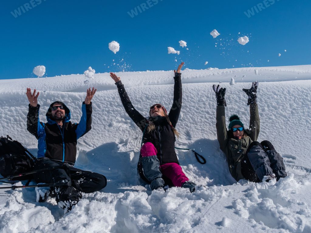 A group of friends lying in the snow wearing winter clothes, throwing snowballs and having fun