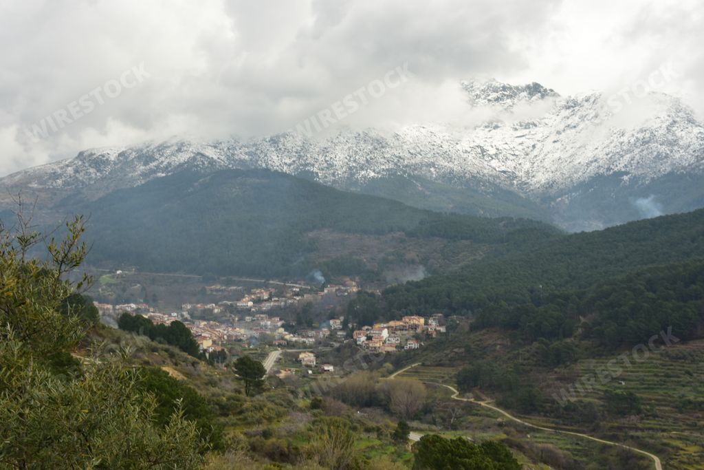 A high angle shot of a village in the valley at the foot of a snow covered mountain