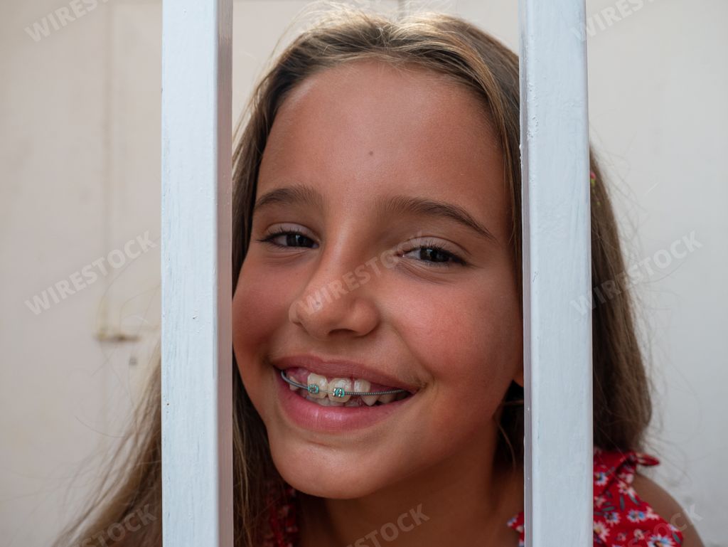 A cute teenage Caucasian smiling girl with braces looking at the camera behind the bars