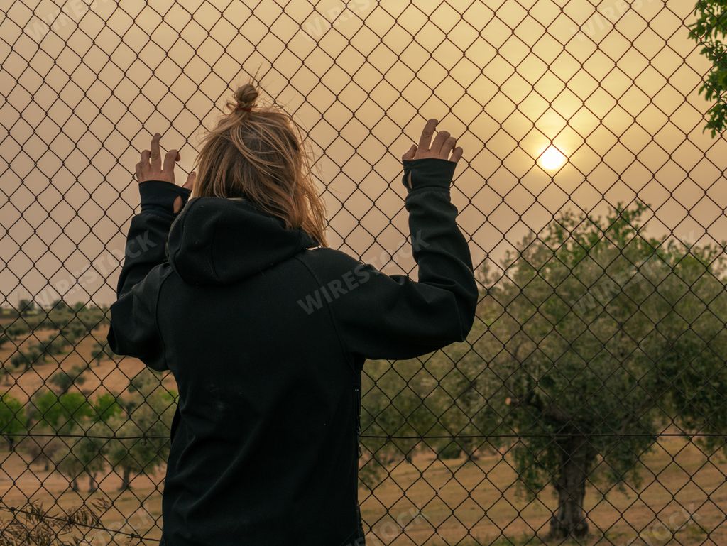 Blond woman leaning on a fence at sunset