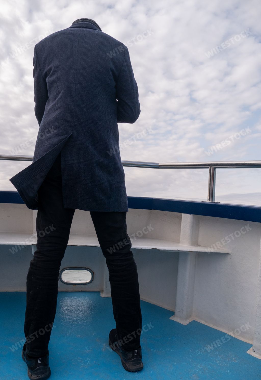 A vertical back view of a male standing on a boat