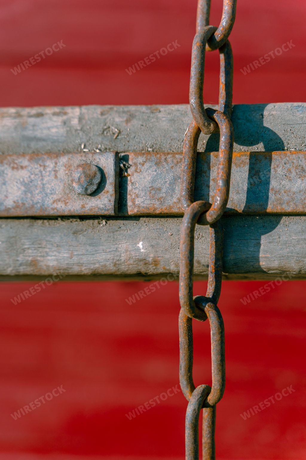 A vertical shot of an old rusty chain of a timber sled in front of a red wooden gate