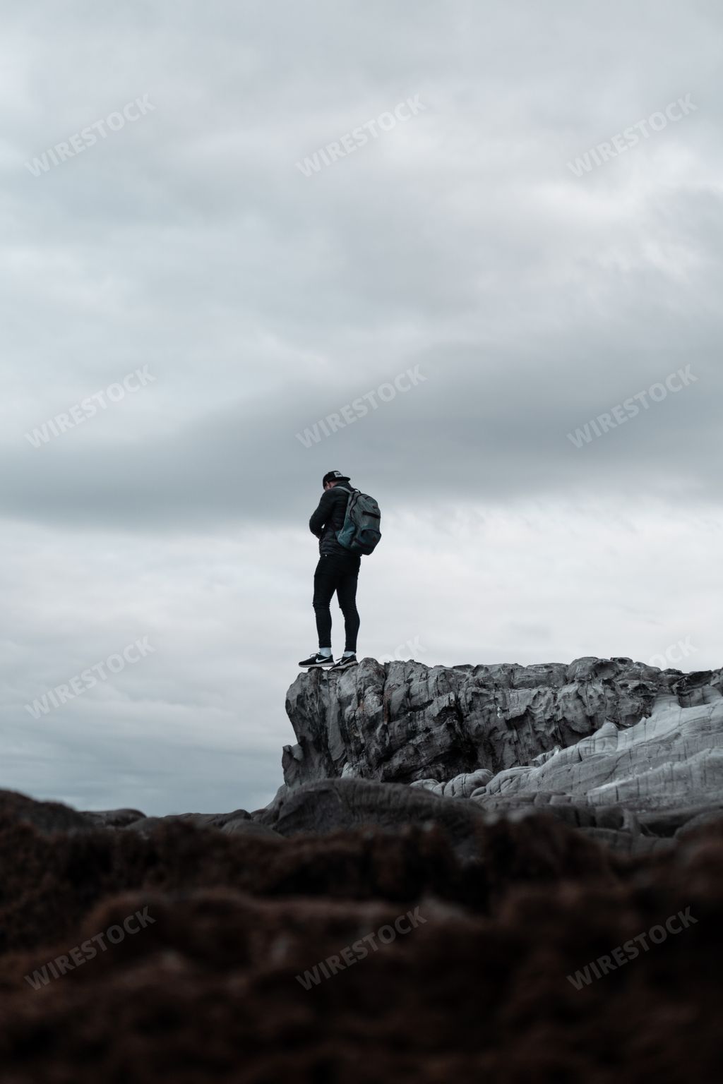 A vertical shot of a person wearing backpack standing at the edge of a gray cliff